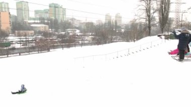 Ukrayna, Kyiv - 30 Ocak 2021: İnsanlar çok katlı bir binanın avlusunda kar tepesinde kayıyorlar. Kışın karlı bir günde plastik bir kızakla kayan çocuklar. Mutlu bir çocukluk. Dışarıda kar yağıyor. Tatil çocukları eğleniyor