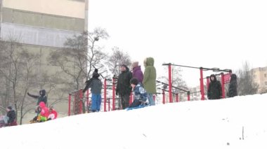 Ukrayna, Kyiv - 30 Ocak 2021: İnsanlar çok katlı bir binanın avlusunda kar tepesinde kayıyorlar. Kışın karlı bir günde plastik bir kızakla kayan çocuklar. Mutlu bir çocukluk. Dışarıda kar yağıyor. Tatil çocukları eğleniyor