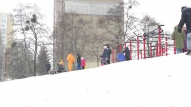 Ukrayna, Kyiv - 30 Ocak 2021: İnsanlar çok katlı bir binanın avlusunda kar tepesinde kayıyorlar. Kışın karlı bir günde plastik bir kızakla kayan çocuklar. Mutlu bir çocukluk. Dışarıda kar yağıyor. Tatil çocukları eğleniyor