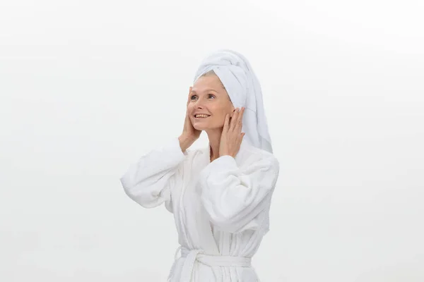 Feminino adulto mais velha mulher vestindo roupão de banho e toalha sobre sua cabeça sorrindo isolado sobre fundo branco — Fotografia de Stock