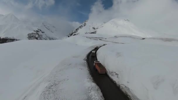 Flygfoto över vackra snöiga berg i Gudauri, Georgien. konvoj av lastbilar som rör sig längs en bergsväg — Stockvideo