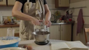 Fırın konseptine yakın çekim - Kadın kakao tozunu metalik süzgeçten pişirmek için cam klozete süzüyor