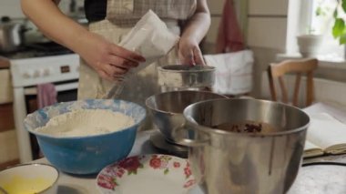 Fırın konseptine yakın çekim - Kadın kakao tozunu metalik süzgeçten pişirmek için cam klozete süzüyor