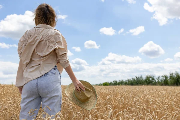 Yazın buğday tarlasında poz veren bir kadın. Elinde altın buğday tarlasının arka planında şapkasını tutan bir kadın. Arkadan manzara..