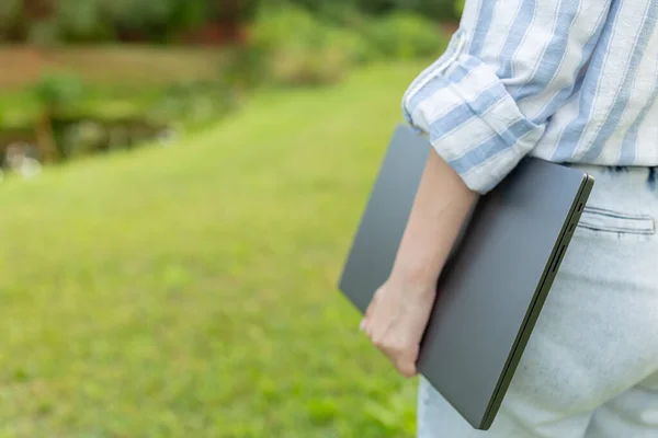 Back view of a woman who is standing with a closed laptop. Rear view people collection. backside view of person outdoor. Young engineer with a closed laptop in hand. Copy space