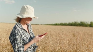 armerwoman in the hat texting on her phone in the gold wheat field during the sunset.