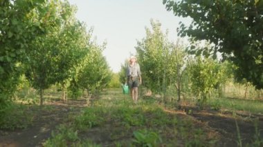 woman farmer walkinfg inspects the gatden. Girl holds watering can in hands for plants. Casual summer rural clothes denim clothes. Agricultural concept