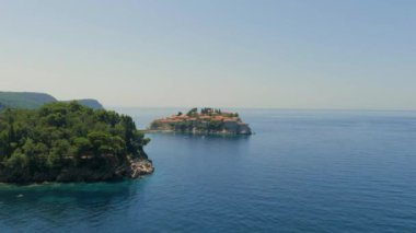 Karadağ. Adriyatik Denizi. Ada ve Sveti Stefan plajı. Yaz. Güneşli bir hava. En iyi sezon. Çok popüler bir turistik yer. Drone. Uçuş. Kamera ileri gidiyor.