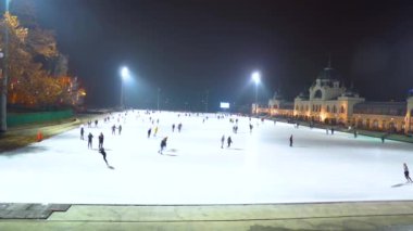 Macaristan. Budapeşte şehri. Kış akşamı. Caddedeki buz pateni pistinin panoraması. İnsanlar paten kayıyor. Kamera soldan sağa hareket ediyor.
