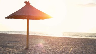 Gün batımında boş kumlu plaj. Sahilde tek bir ahşap plaj şemsiyesi var. Sabit Kamera