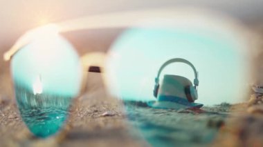 Gün batımında boş kumsal (gündoğumu). Aynalı güneş gözlükleri plajda yatıyor. Yansımada bir şapka ve kulaklık görünür. Sabit Kamera