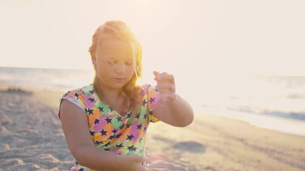 日の出 に空の砂浜 少女は海岸に座り 砂を手から手に注ぐ 固定カメラ — ストック動画