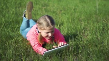 Bahar. Güneşli bir hava. Yeşil çimenli tepe. Kız elinde tabletle çimlerin üzerinde yatıyor. Sabit Kamera