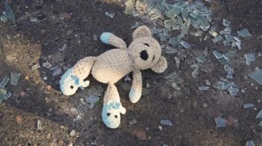 Ukrayna 'da savaş. 2022 Rus istilası Ukrayna. Bir oyuncak (oyuncak ayı) kırık camın arka planında kaldırımda yatar. Adam (yakın çekim el) çerçeveden bir oyuncak ayıyı alır