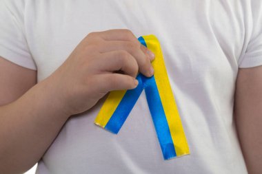 Beyaz tişörtlü bir kız elinde sarı-mavi bir tekstil kurdelesi tutuyor. Ukrayna bayrağı. Ukrayna 'nın ulusal sembolü. Vatansever. Yakın plan.