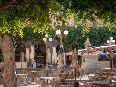 Empty cafe and restaurant terrace with potted plants, trees, tables and chairs in Valletta, Malta