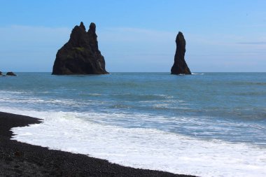 Güney İzlanda, Vik yakınlarındaki siyah kumsalda bazalt yığınları, Reynisdrangar sütunları, yağmurlu mavi gökyüzü manzarası.