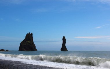 Güney İzlanda, Vik yakınlarındaki siyah kumsalda bazalt yığınları, Reynisdrangar sütunları, yağmurlu mavi gökyüzü manzarası.
