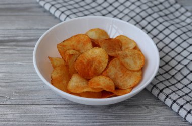 Gümüş bir masada kırmızı biberli lezzetli patates cipsli kase.