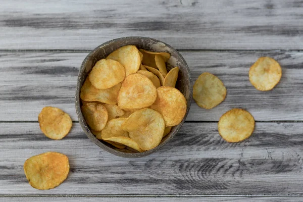 Hasır bir kasede patates cipsi, eski masanın üstünde.
