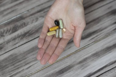 Ahşap bir masanın zemininde haplar ve haplar tutan bir kadın. Vitaminli el.