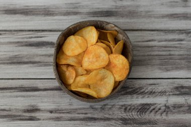 Eski mutfak masasında bir hasır kase gevrek patates cipsi