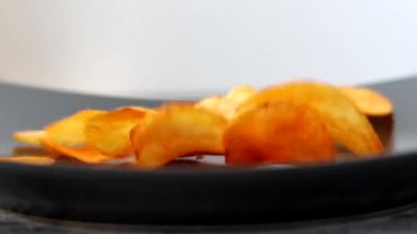 Patates cipsi siyah tabağa düşüyor. Cipsler kırmızı biber aromalı. 4k