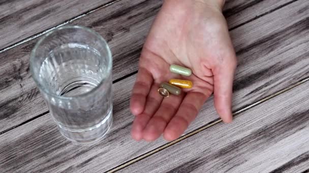 De vrouw houdt haar medicijnen, vitaminen en pillen in haar hand en drinkt elk op zijn beurt. Een jonge vrouw neemt haar medicijnen. Gezondheidszorg, farmacie, het begrip behandeling. — Stockvideo