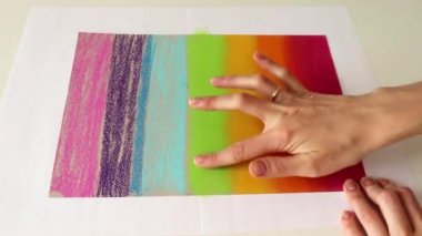 Sanatçılar kağıt üzerine pastel boya kalemleriyle gökkuşağı renkleri çizerler.