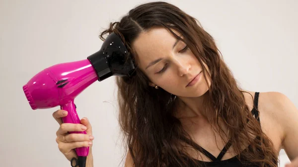 A young woman is styling her curly, wavy hair with a special diffuser hair dryer attachment