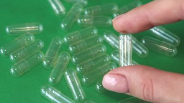 A woman holds an empty capsule in her hand against a green background