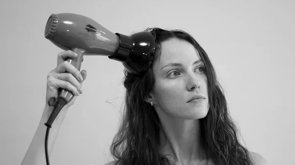 A woman with curly hair dries her hair with a hair dryer with a diffuser attachment. Black and white photo.
