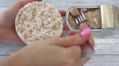 A womans hand smears cod liver on rice bread. Eat a can of cod liver, oil rich in vitamin d