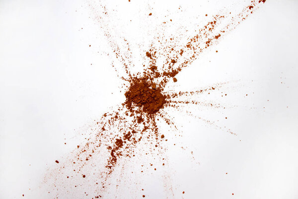 Carob powder on a white sheet of paper. Explosion on the white background above. Carob scattered with a copy of the space.