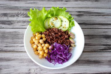 Buddha bowl with vegetables, chickpeas, red cabbage, lettuce, red rice, zucchinipi, stachios on wooden background.