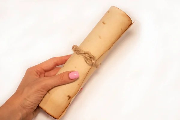 Scroll of ancient paper in a womans hand on a white background, laid at an oblique angle.