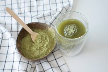 Matcha green tea powdered and brewed on a white background with a white checkered kitchen towel