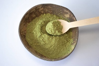 Woman scoops matcha green tea powder into a wooden spoon on a white background