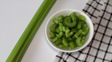 Celery slices in a small white bowl on a white plate with a napkin. Green slices of celery. Top view