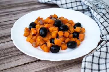 Ahşap bir zeminde beyaz bir tabakta zeytin ve soğanlı fırında tatlı patates.