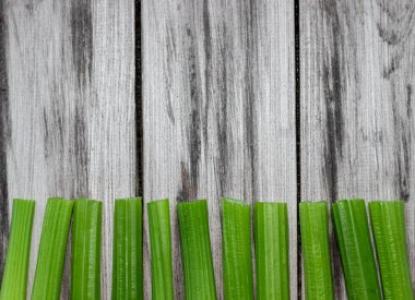 Kahverengi arka planda yan yana sıralanmış yeşil kereviz sapları. Sağlıklı beslenme konsepti, yiyecek temeli. Metin için alanı olan sebze çerçevesi