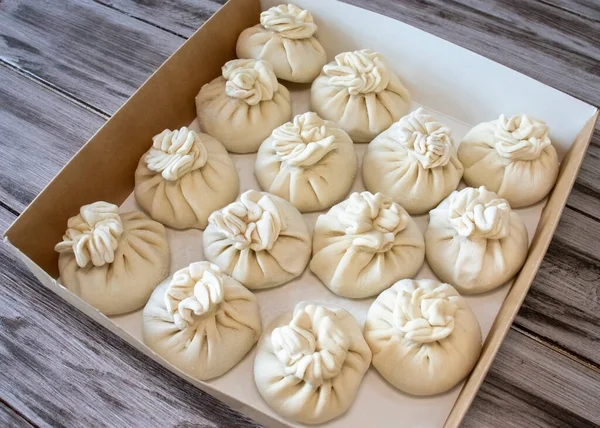 Frozen khinkali with meat in a cardboard box on a wooden background