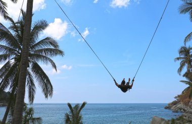 Salıncakta sallanan genç bir adam okyanus ve denizin arka planına karşı. Bulutların arka planı. Arkadan sallanan adam. Tayland 'da Tatil