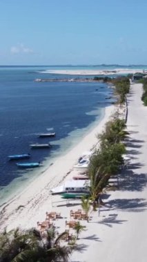 Okyanus kıyısındaki kumlu bir yolun üzerindeki bir uçuşun havadan görüntüsü. Tekneler ve ada manzarası. Dikey video.