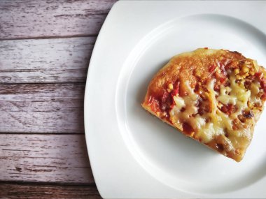 Beyaz bir tabakta pizza diliminin üst görüntüsü. Pizza soslu, peynirli, domatesli, etli ve çeşitli otlarla kaplı.