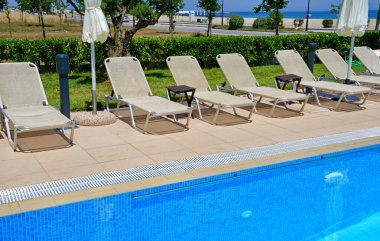 Güneşte ve mavi gökyüzünde bir yüzme havuzunun kenarında uzanırlar.