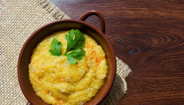 Mısır lapası, çatırtı, havuç, soğan ve bitkilerle. Tahta bir masada seramik bir tabakta.