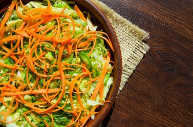 Taze sebze salatası. Masadaki seramik tabakta havuç, taze lahana ve yeşiller..