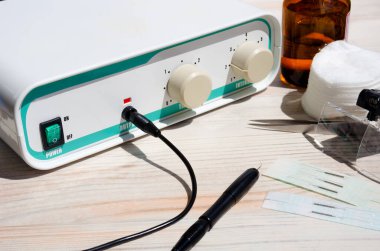 Elektrikli epilatör, alkol, iğneler, tüy dökücü cımbızlar. Beyaz masadaki insanların kıllarını almak için bir cihaz..