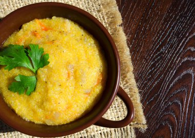 Mısır lapası, çatırtı, havuç, soğan ve bitkilerle. Tahta bir masada seramik bir tabakta.